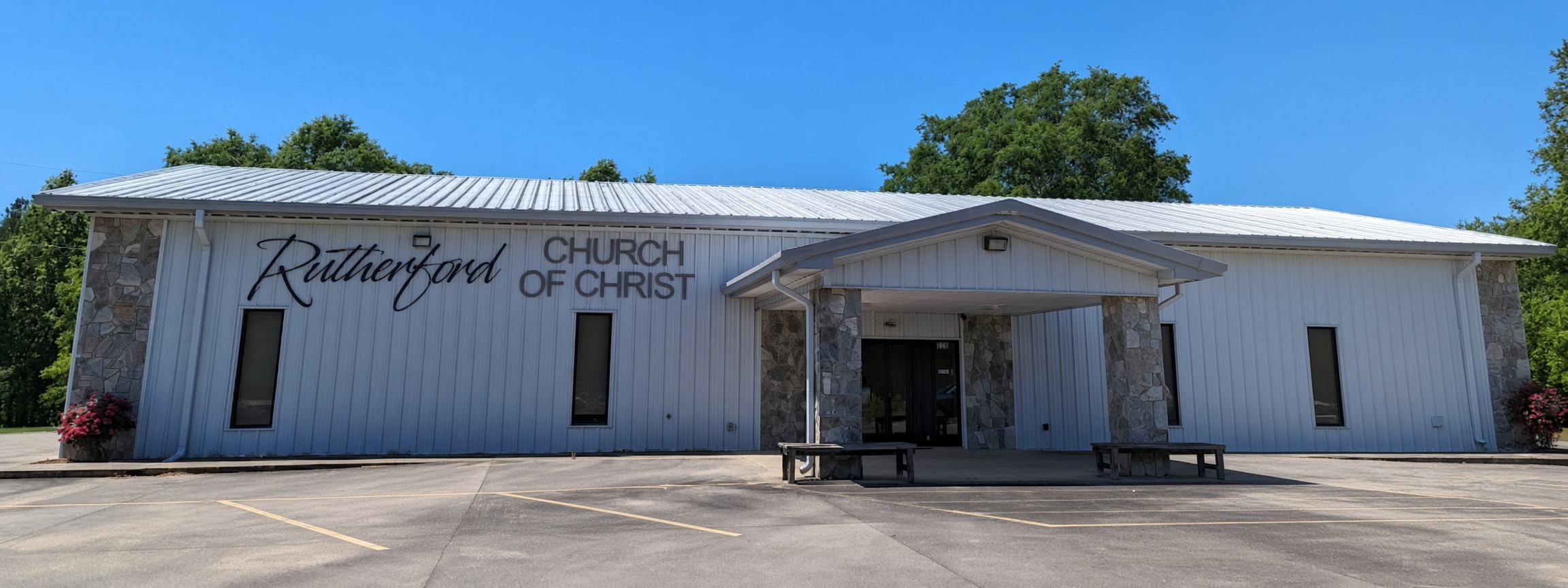 The exterior of the Rutherford Church of Christ building featuring white siding and stone accents under a clear blue sky.